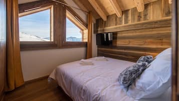 Ein Schlafzimmer mit Bett, einem Fenster mit Bergblick, Holzwänden und einem an der Wand befestigten Flachbildfernseher.