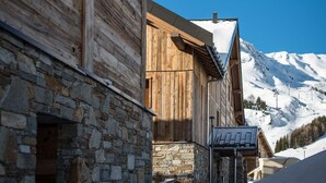 A wooden building with stone walls, a sloped roof, and a view of snow-covered mountains.