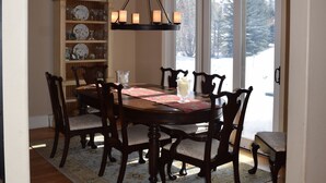 A dining room with a wooden table and chairs, a chandelier, and a bookshelf. - Vail - Club at Cordillera Mountain Home with Exclusive Golf/Ski Privileges (Cordillera)