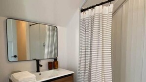 Un baño con tocador de madera, un espejo, una pila de toallas y una cortina de ducha a rayas.
