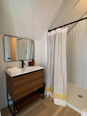 Une salle de bain avec un meuble-lavabo en bois, un miroir, une pile d’essuie-baignette et un rideau de douche à rayures.