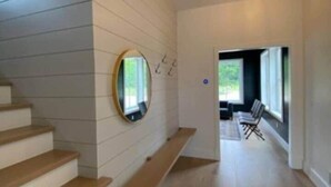 A modern interior with a wooden staircase, a round mirror, and a view into a living area. - Ellison Bay Family Retreat! 8 bed/6 bath/20 acres (Ellison Bay)
