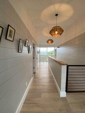 Un couloir doté d’un plancher en bois, de tableaux encadrés accrochés aux murs et d’un éclairage suspendu.