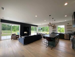 Une cuisine moderne dotée d’un grand îlot central, de meubles de rangement aux couleurs sombres et d’un coin repas avec une table et des chaises hautes.