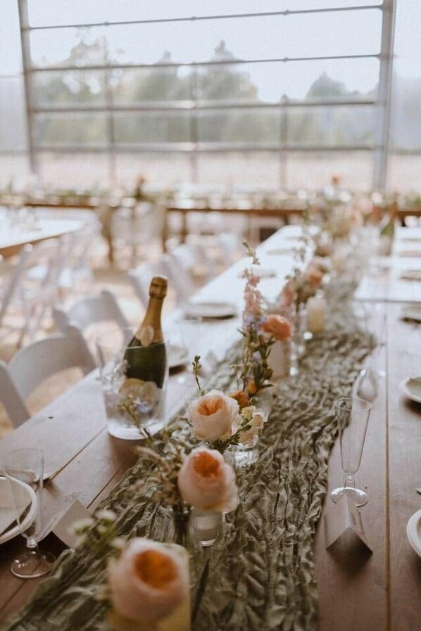 Une longue table agrémentée d’un centre de table décoratif, de verres et d’une bouteille.