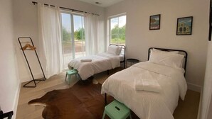 Un dormitorio con dos camas, una silla colgante y un taburete pequeño.