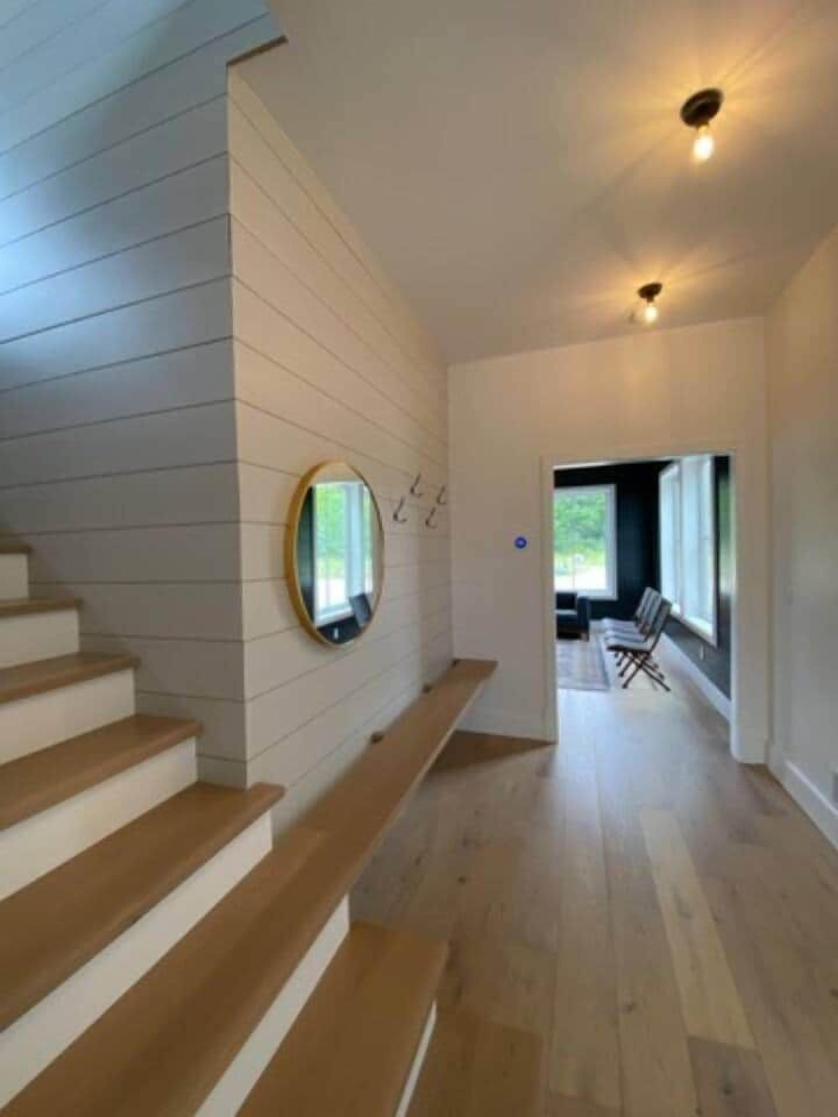 Ein modernes Interieur mit einer Holztreppe, einem runden Spiegel und Blick in einen Wohnbereich.