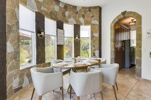 A stone-walled dining area with a round table set for six, surrounded by white chairs.