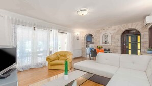 Una sala de estar moderna con un sofá, un sillón amarillo, una mesa de centro de vidrio y un televisor.
