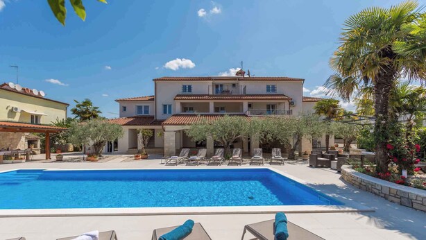 Un hotel con piscina, sillas de descanso y un edificio grande con balcones.