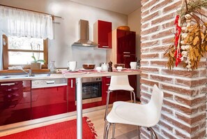 A modern kitchen with red cabinetry, a brick accent wall, and white chairs.