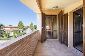 A balcony with a brick wall, a tiled floor, and a view of houses and trees.