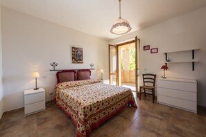 Une chambre à coucher comprenant un lit, des tables de chevet, une chaise, un bureau et une porte donnant sur un balcon.