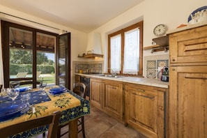 A kitchen with wooden cabinets, a tiled backsplash, and a dining table set for two. - Villa Clemente by MMega (Lucignano)