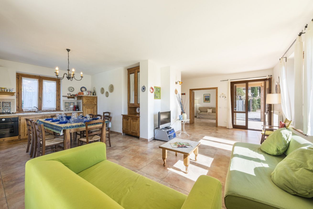Un'ampia zona giorno con un divano verde, un tavolo da pranzo e una cucina sullo sfondo.
