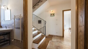 Un escalier menant à un deuxième étage, une salle de bain avec un lavabo et un porte-serviettes, et un sol carrelé.