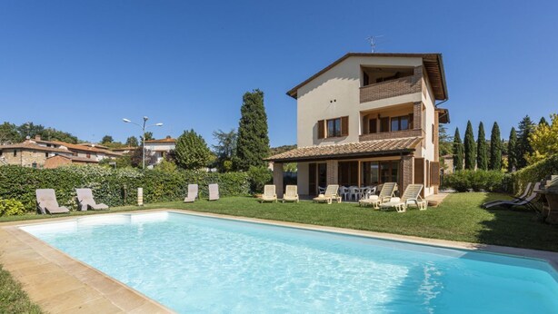 Une maison à deux étages avec une piscine, des chaises longues et un jardin bien entretenu.