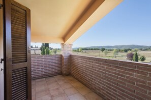 Ein Balkon mit einer Ziegelwand, einer Holztür und Blick auf eine grüne Landschaft.