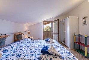 Ein Schlafzimmer mit Bett, Nachttisch, Lampe, Kleiderschrank und Blick ins Freie.