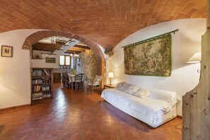 A room with a brick ceiling, a white sofa, a dining table with chairs, a bookshelf, and a painting on the wall.