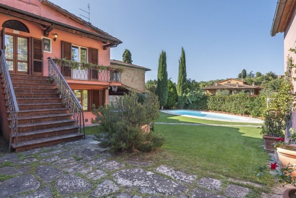 Una casa de dos pisos con una escalera de piedra, piscina y césped bien cuidado.