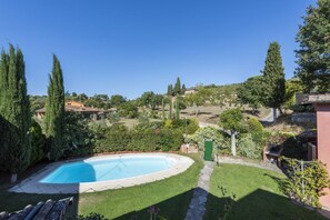 Una piscina rodeada de césped cuidado y árboles, con vista a una colina y edificios al fondo.