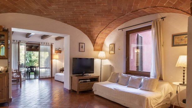 Quarto aconchegante com televisão, sofá, luminária e janela com persianas.