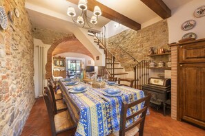Un comedor con pared de piedra, vigas de madera, una escalera y una mesa preparada para una comida.