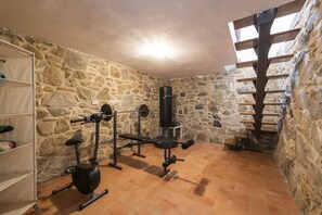 A stone-walled room with a weight bench, an exercise bike, and a punching bag.