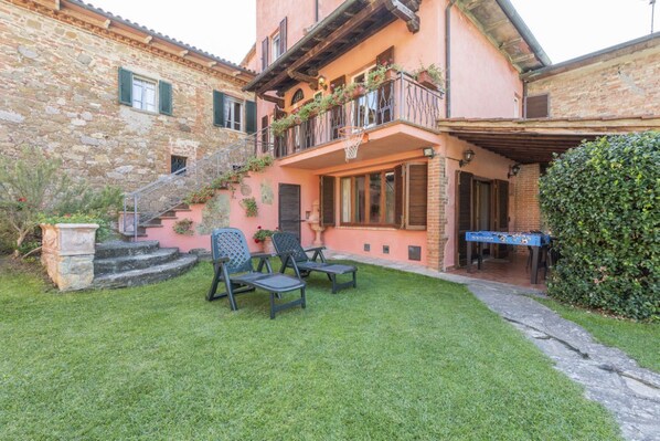 A stone building with a balcony, a small outdoor seating area with chairs, and a table.