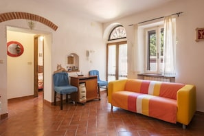 Una sala de estar con sofá, escritorio, silla, espejo y ventana con cortinas.