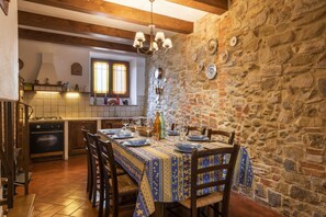 Un coin repas rustique avec un mur en pierre, des poutres en bois et un sol carrelé.