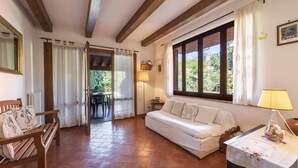 Quarto com um banco de madeira, um sofá branco, uma mesa com abajur e vista pela janela grande.
