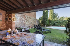 An outdoor patio with a tiled table, chairs, and a brick wall.