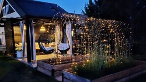 Una casa con porche cubierto, una hamaca colgante y un jardín con luces de cuerda.