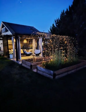 A house with a covered porch, a hanging chair, and a garden with string lights.