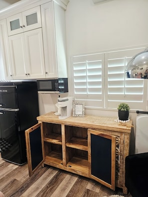 Una cocina con armarios blancos, un refrigerador negro, una cafetera y una mesa de madera con una planta en maceta.