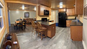 A compact kitchen with wooden cabinets, a black refrigerator, and a microwave. There is a dining area with a table and chairs. - Spacious 3 bedroom 2 bath lodging near trails, with lots of off-street parking! (Ely)