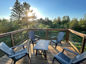 A wooden deck with four Adirondack chairs and a small table, surrounded by a wooden railing and a metal fence. - Spacious 3 bedroom 2 bath lodging near trails, with lots of off-street parking! (Ely)