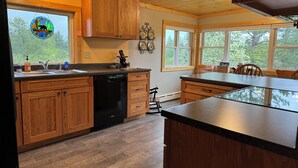 A kitchen with wooden cabinets, a dishwasher, and a large window with a view of trees. - Spacious 3 bedroom 2 bath lodging near trails, with lots of off-street parking! (Ely)