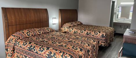 A hotel room with two beds, a small desk, and a chair.