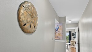 A hallway with a textured wall art piece, a painting of a bird, and a view of a balcony with outdoor furniture.
