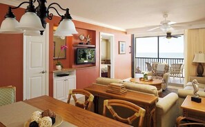 Enjoy a serene ocean view from the comfort of this well-appointed living room, featuring a dining table for four, comfortable seating, and a ceiling fan for a cozy atmosphere.