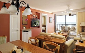 Enjoy a serene ocean view from the comfort of this well-appointed living room, featuring a dining table for four, comfortable seating, and a ceiling fan for a cozy atmosphere.