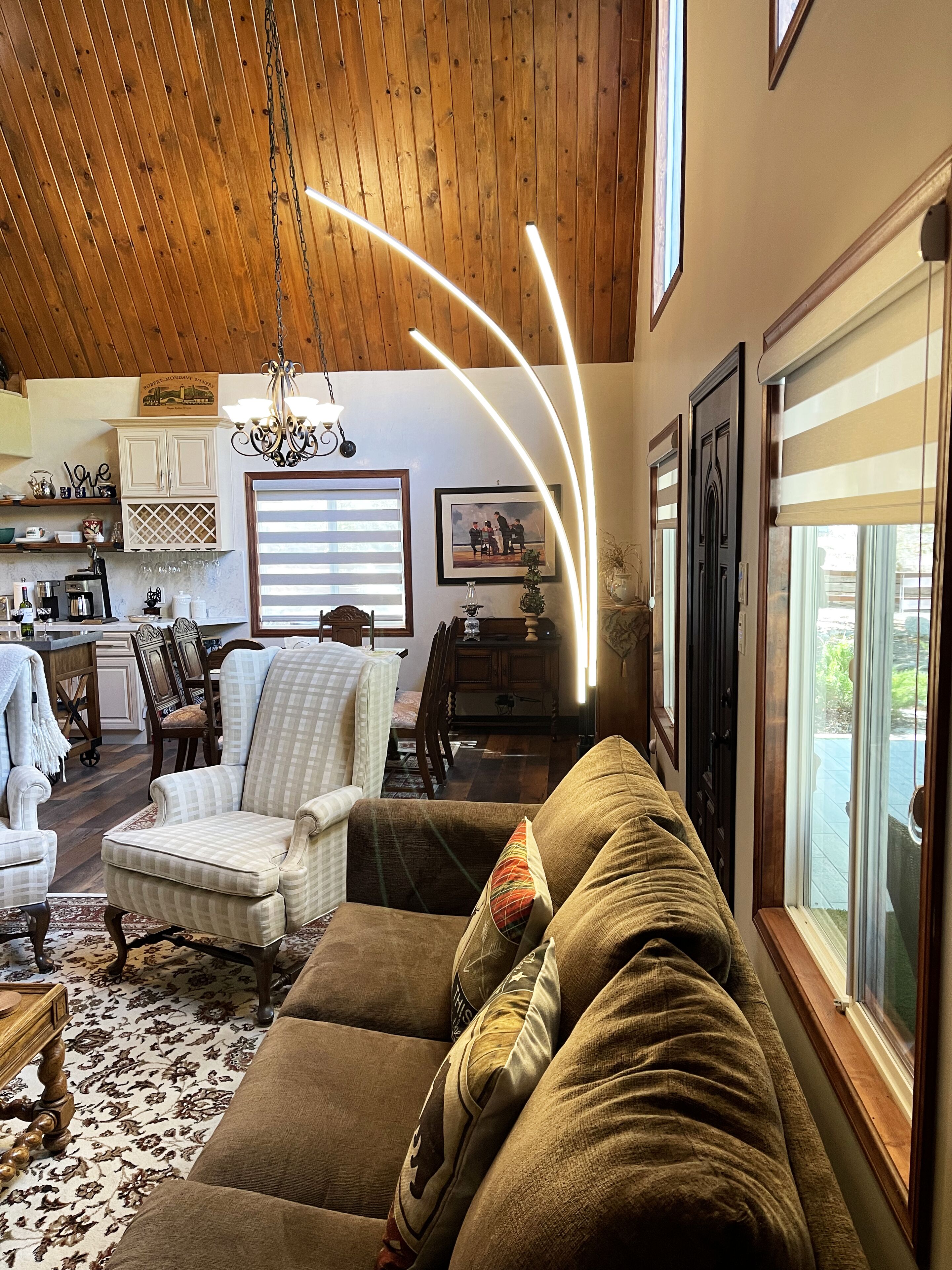 A cozy living room with a wooden ceiling, a sofa, a chair, and a dining area with a table and chairs.