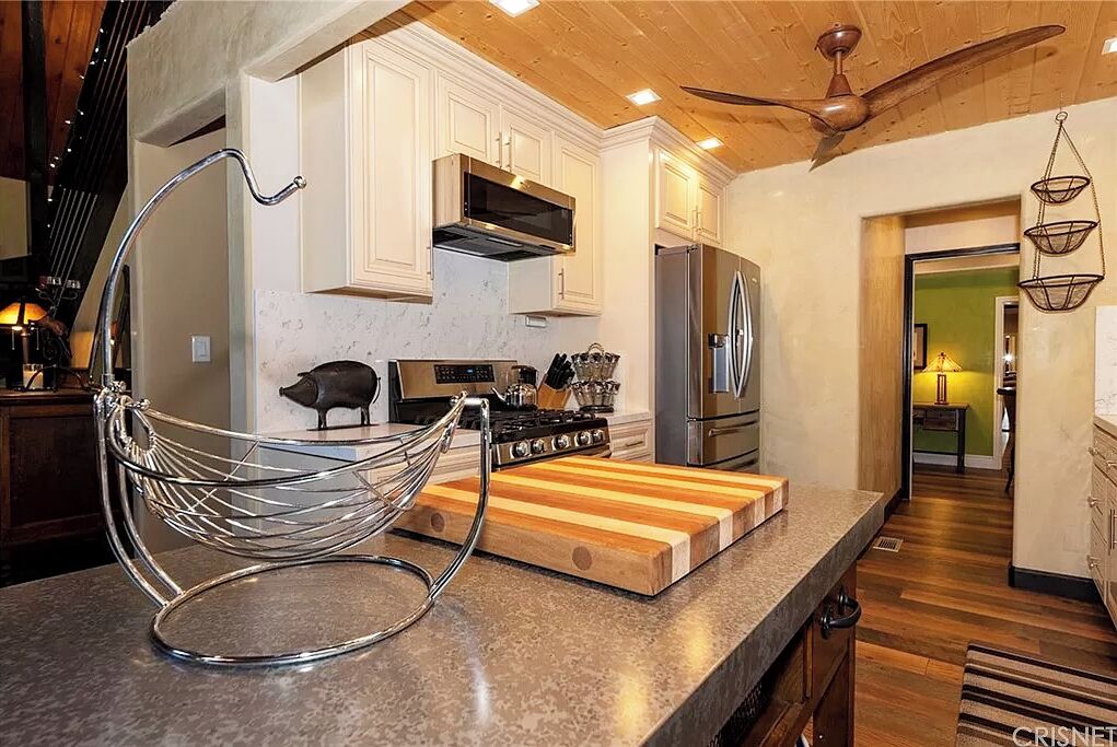 Una cocina moderna con armarios blancos, electrodomésticos de acero inoxidable, encimera de madera y una lámpara colgante.