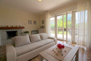 A living room with a sofa, a fireplace, a table with a vase of flowers, and a view through large sliding doors. - Holiday apartment only 200m from the beach (Funtana)