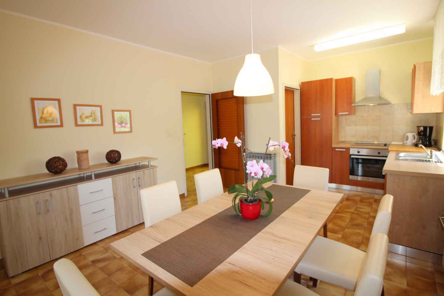 A modern kitchen with a built-in oven, a dining area with a wooden table and chairs, and a kitchen counter with a sink.