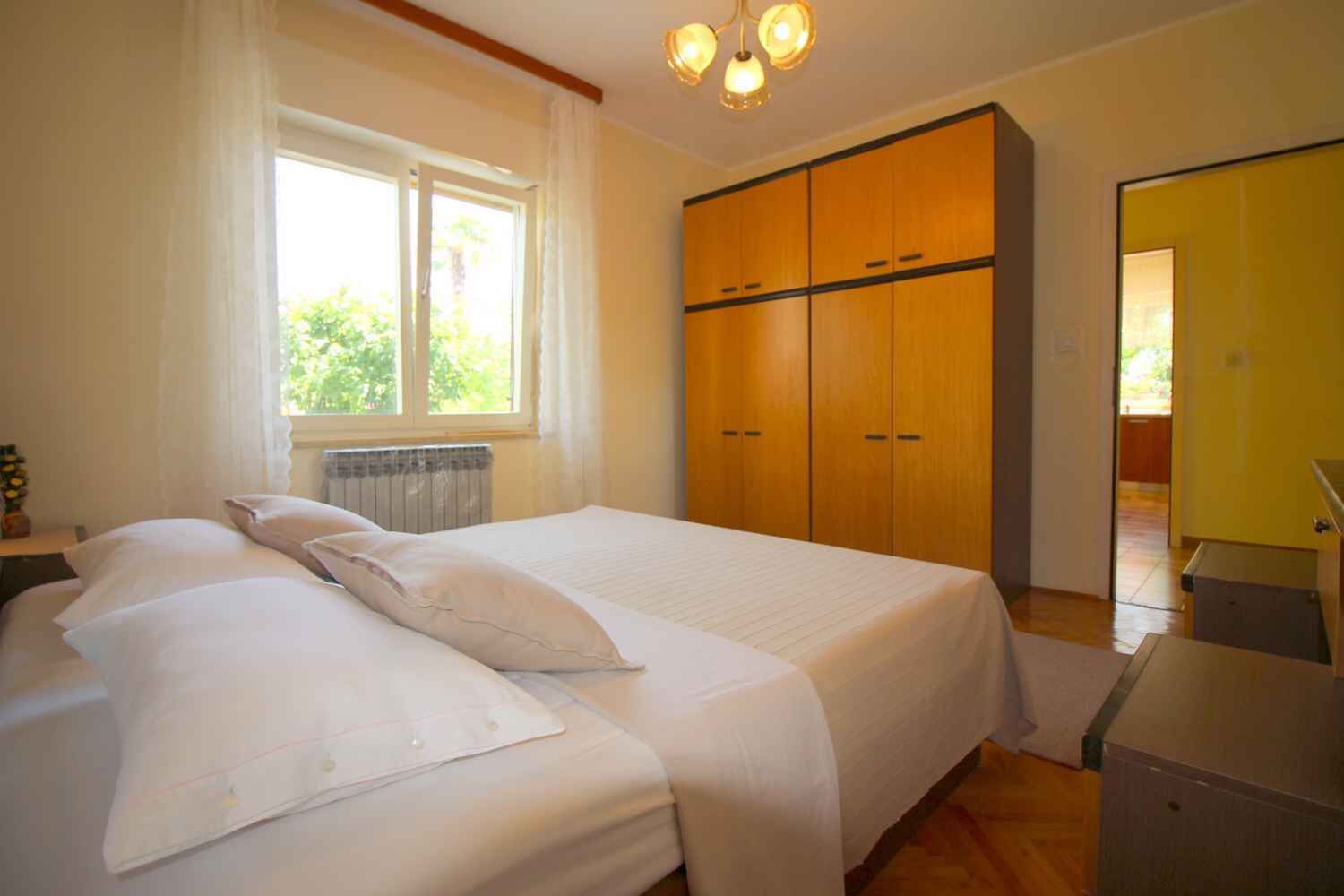 A bedroom with a bed, a window, a wardrobe, and a desk.