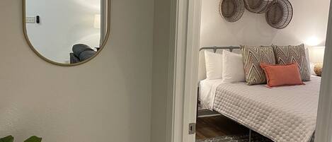 A bedroom with a bed, a mirror, a wall-mounted decorative item, and a potted plant.
